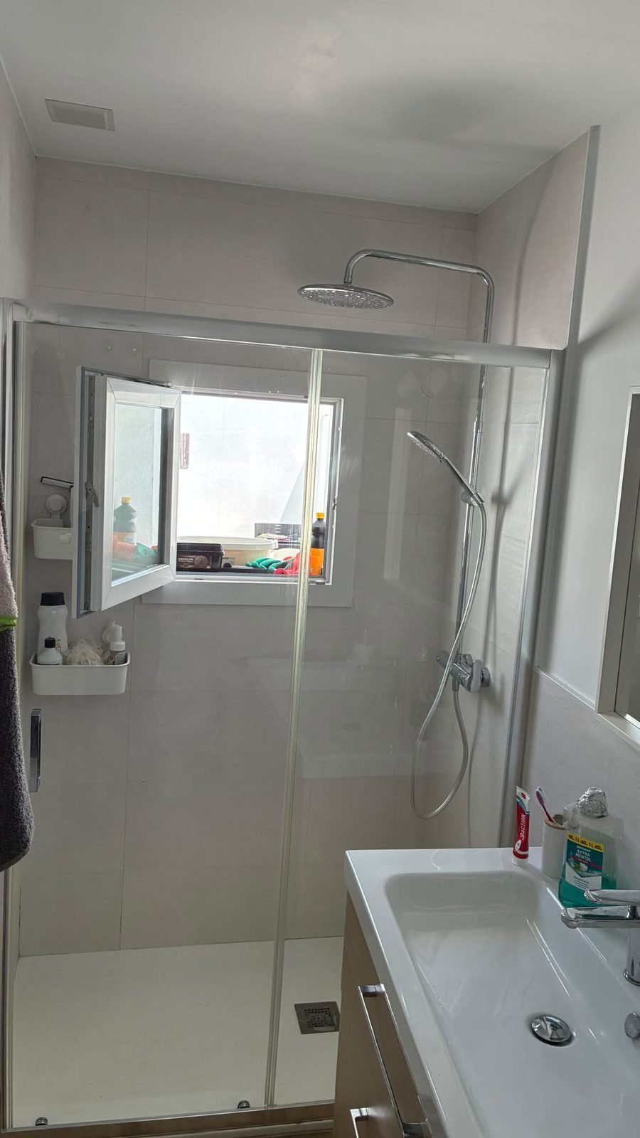 Baño con ducha de mampara, ventana y lavabo
