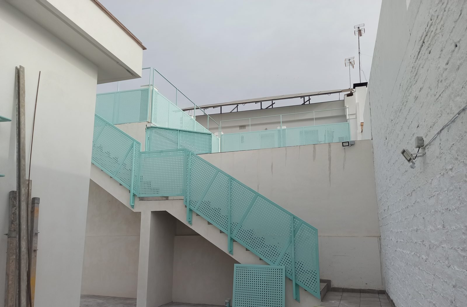 Escalera exterior con barandilla verde agua que sube a la planta alta