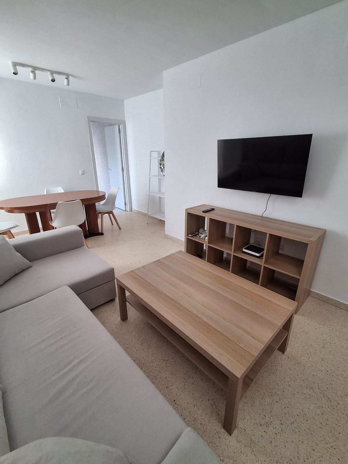 Salón con sofá claro, mueble de televisión y mesa de comedor