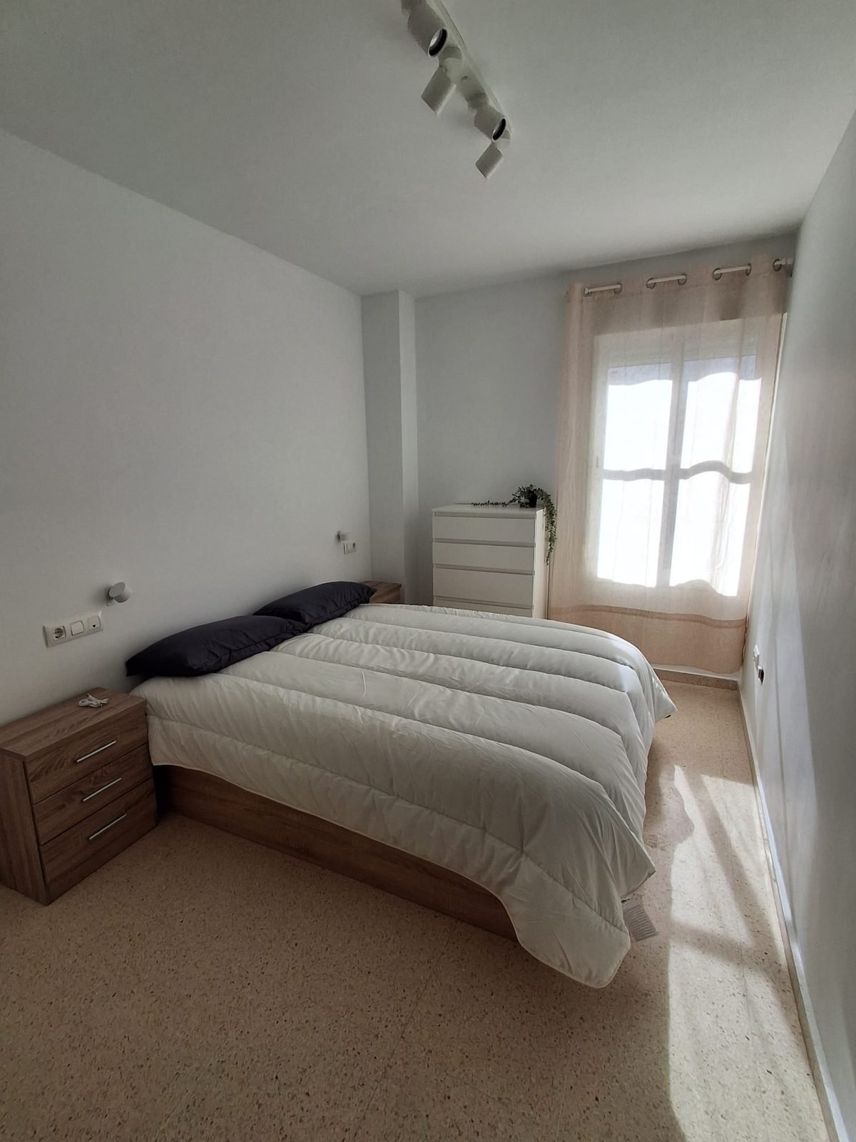Dormitorio con cama de matrimonio, mesilla y ventana
